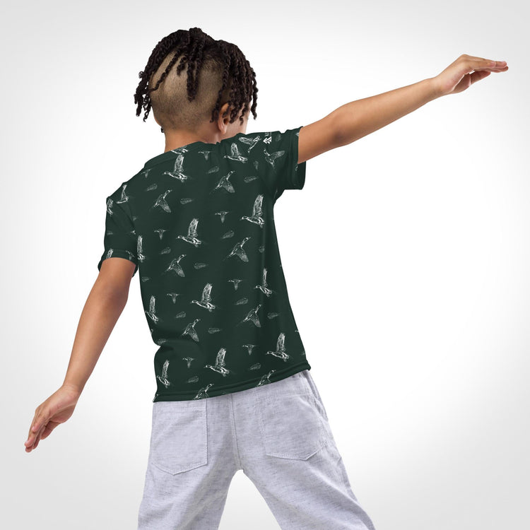 Child wearing a green shirt with a flying ducks pattern, playfully pretending to fly.