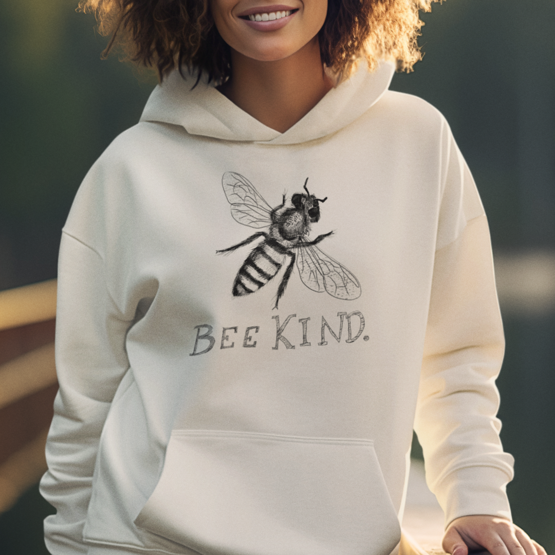 Woman wearing sand-colored Bee Kind hoodie with an illustrated bee design, cute graphic sweatshirt for nature lovers and kindness gifts.

